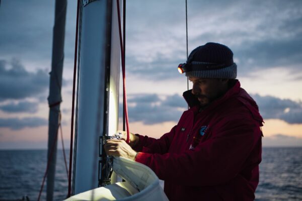 Marin ajustant une voile au crépuscule en mer.