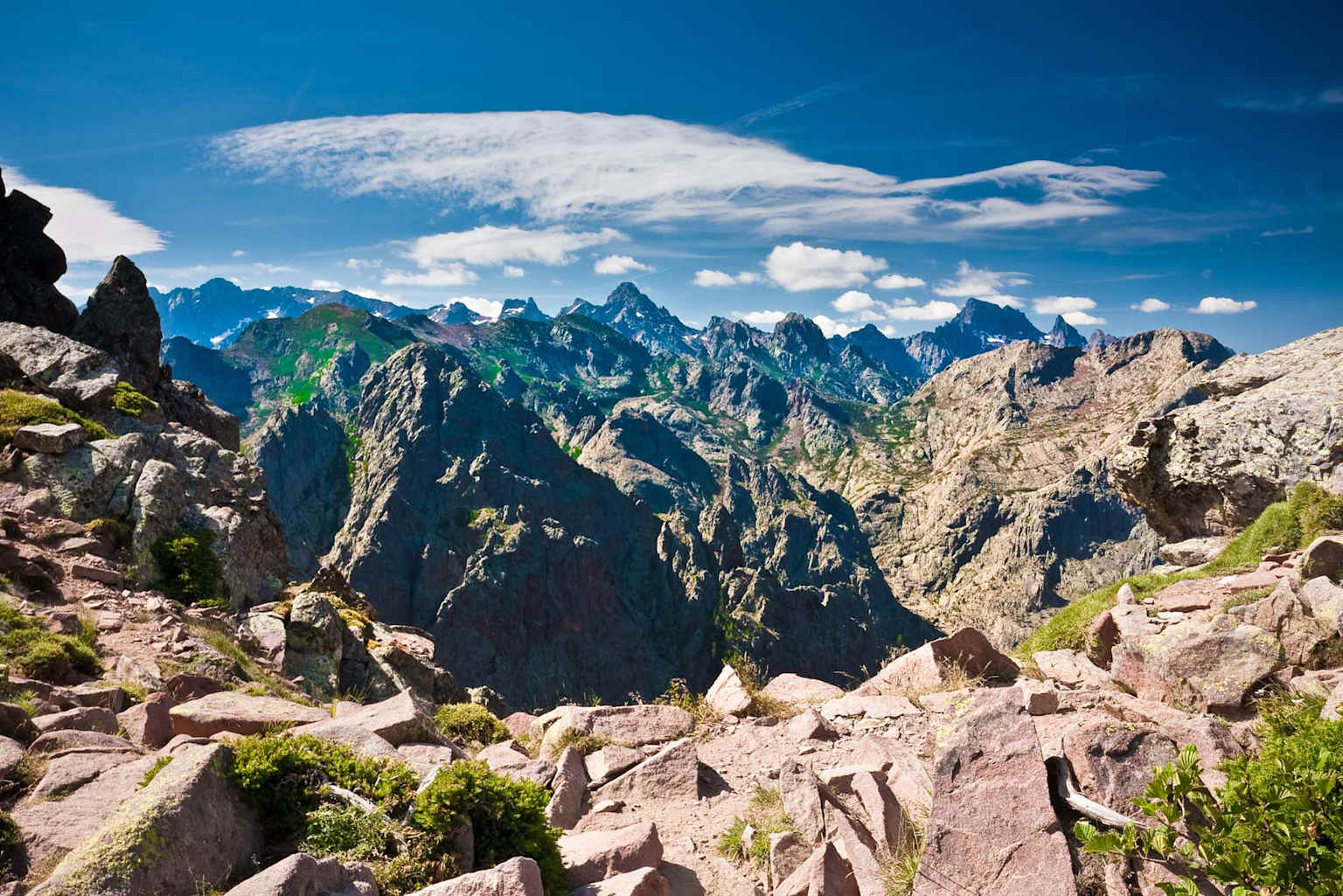 Vue panoramique des montagnes escarpées le long du sentier de randonnée GR20 en Corse sous un ciel bleu clair