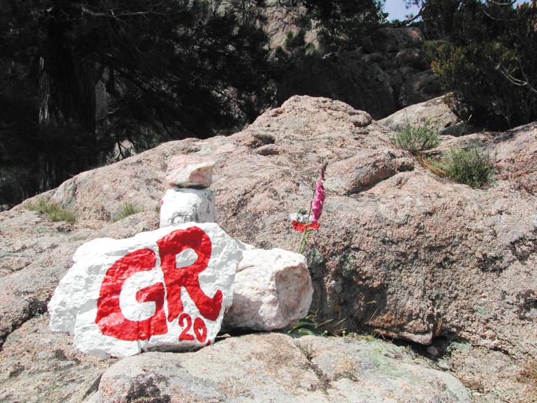 Rocher blanc peint avec un marquage rouge GR20 sur le sentier rocheux corse indiquant l'itinéraire de randonnée GR20
