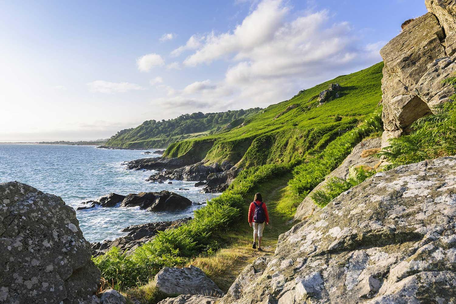 Un randonneur parcourt le sentier côtier verdoyant GR223 le long du littoral normand avec des falaises rocheuses et la mer à proximité